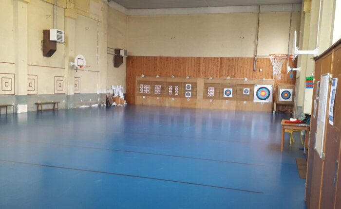 Intérieur du gymnase De Gaulle. Cibles de tir à l'arc, paniers de basket, bancs.
