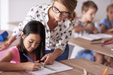Professeure et jeune élève consultant un carnet de cours au sein d'une salle de classe.