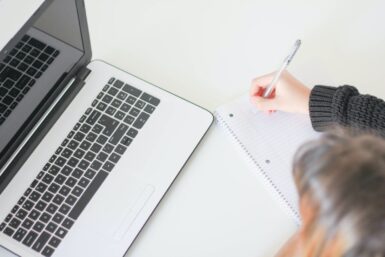Femme prenant des notes devant son ordinateur.