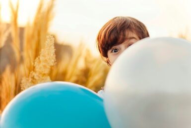 Enfant se cachant derrière 2 ballons gonflables.